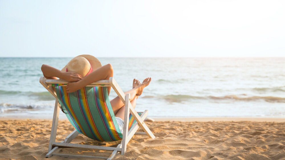 Sommerurlaub am Strand, Frau mit Hut entspannt sich auf einem Liegestuhl am Strand.