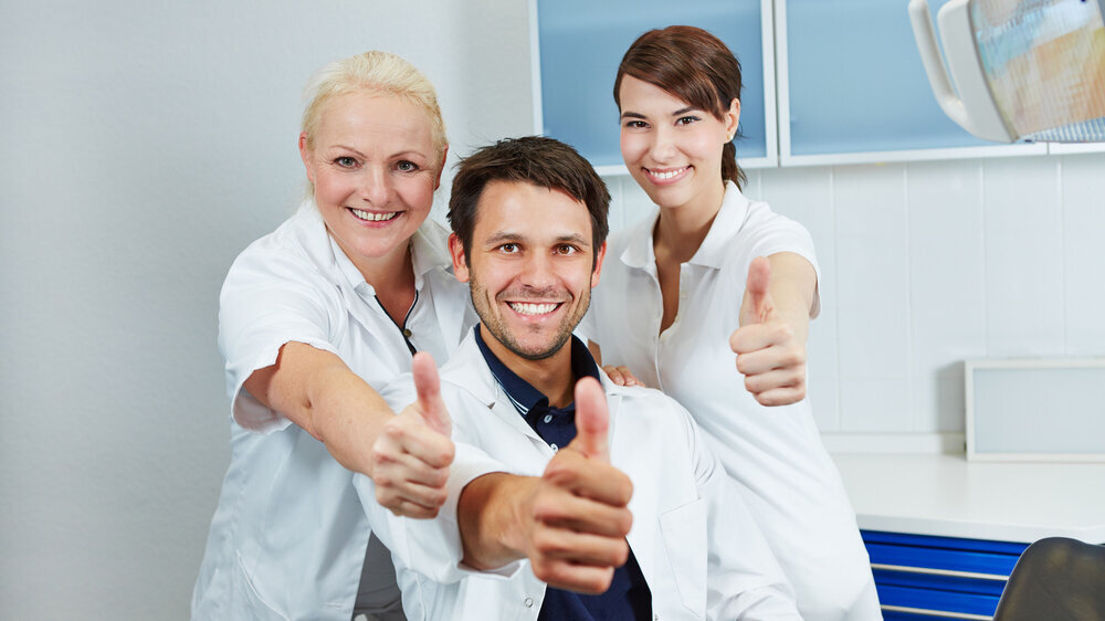 Glücklicher Zahnarzt und lachendes Team hält die Daumen hoch