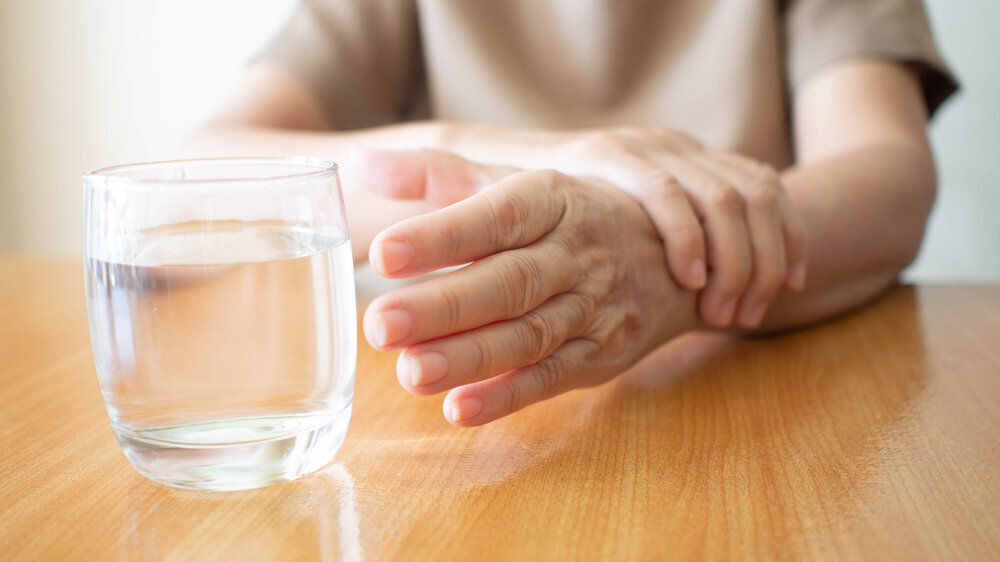 Elderly woman hands tremor symptom reaching out for a glass of water on wood table Elderly woman hands tremor symptom reaching out for a glass of water on wood table