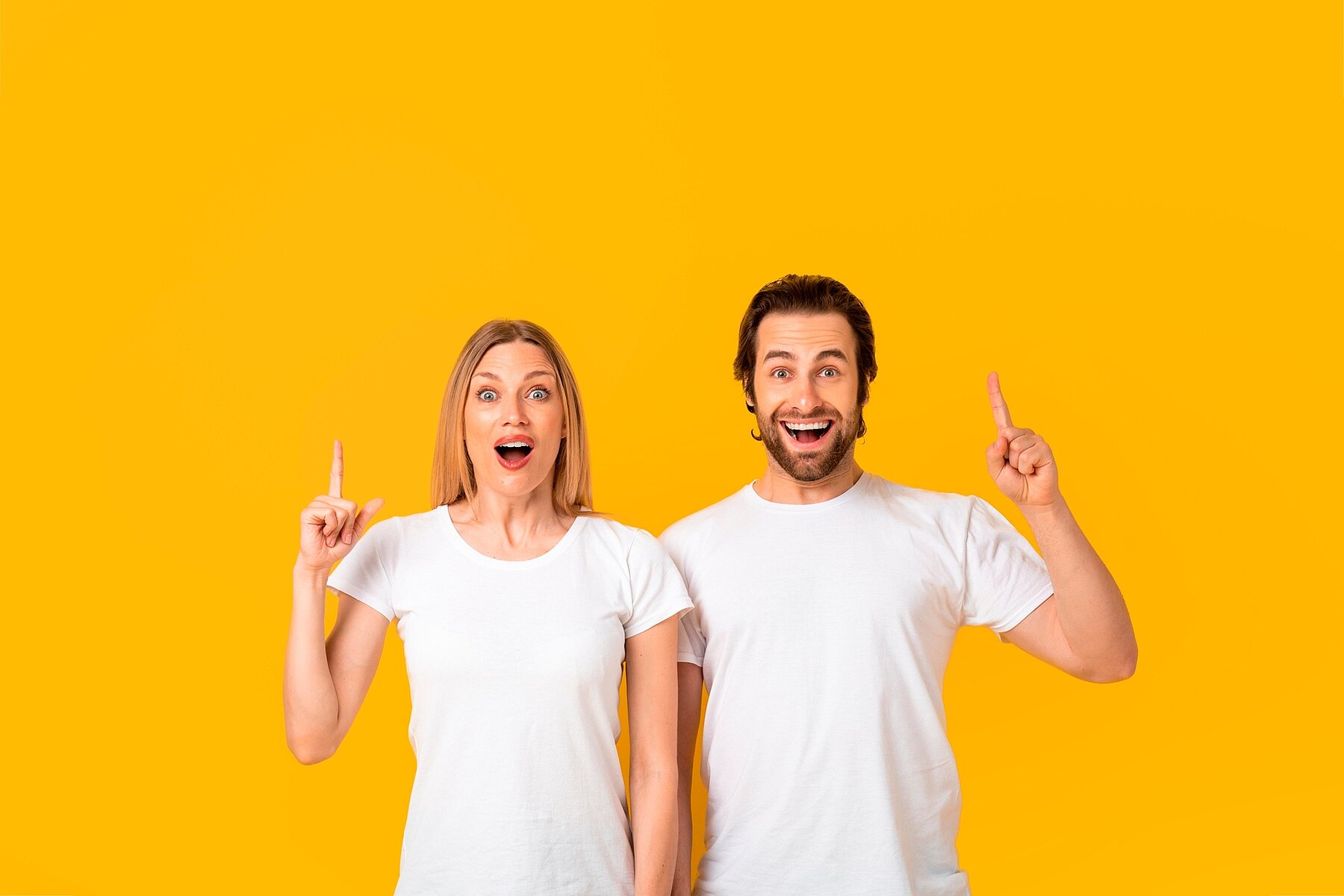 Happy Mixed Gender Couple Smiling And Pointing Upward, Yellow Background, Excitement Concept Excited Happy Mixed Gender Couple Smiling And Pointing Upward At Yellow Background, Engaging In Playful Communication, Capturing Joyful Emotion Expressing Enthusiasm In Studio Setting.