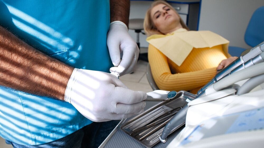 Dentist preparing for the medical examination with young woman patient wearing medical gloves in the dental office. Young female patient sitting on chair in dental office. Hitzeschutz in der Zahnarztpraxis