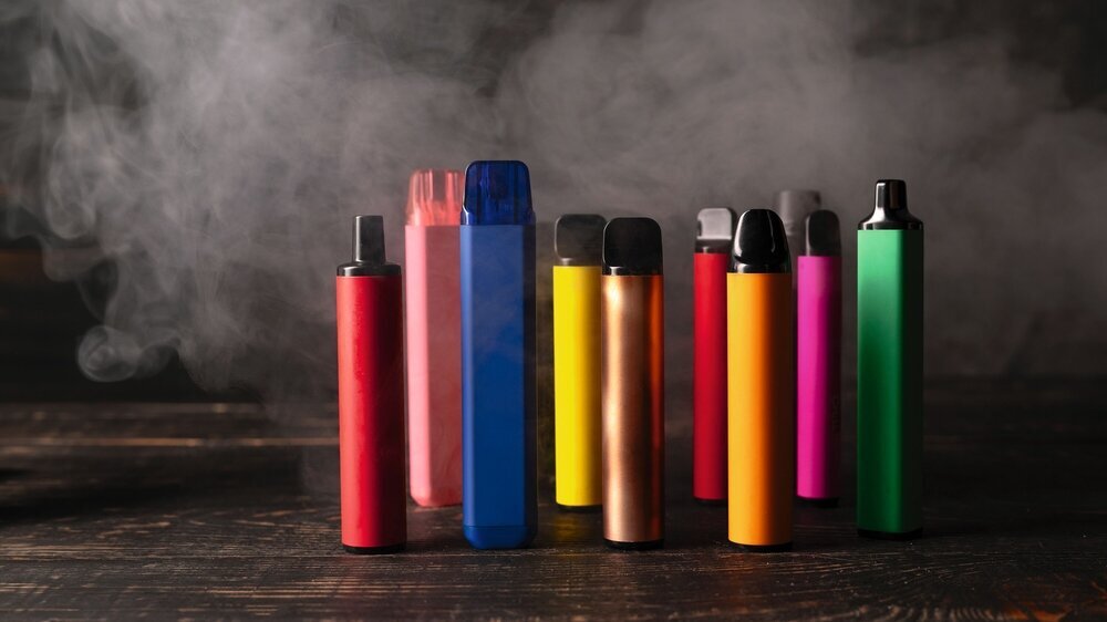 Set of colorful disposable electronic cigarettes on a dark wood background with smoke. Einweg-E-Zigaretten