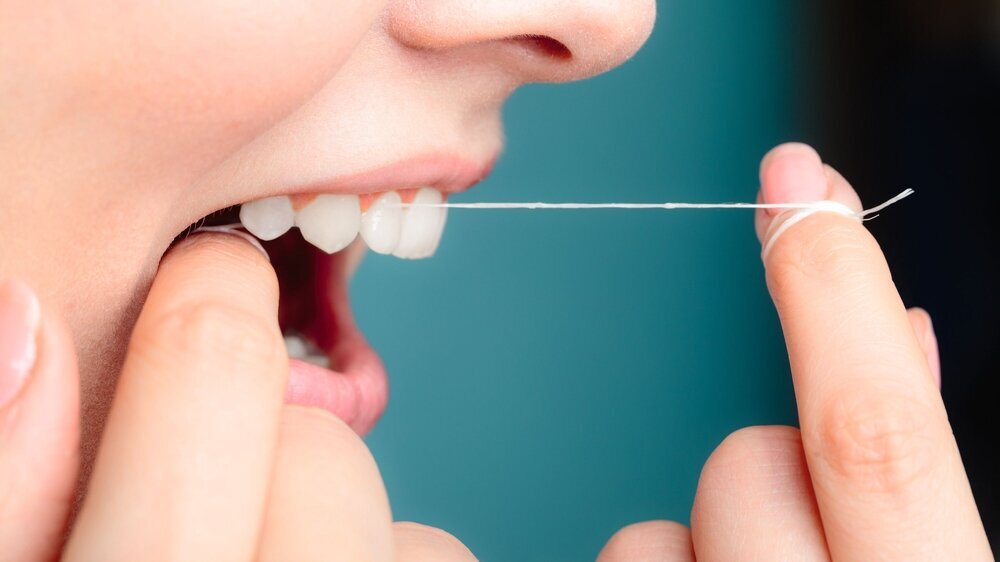 side view woman face smiling with dental floss. Wenn die Zahnseide butterweich flutscht, könnte es an Per- und polyfluorierten Alkylsubstanzen (PFAS) liegen, die mit zahlreichen gesundheitlichen Problemen in Verbindung gebracht werden..