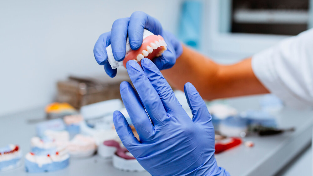 Dental prosthesis, prosthetics work. Close up of prosthetic's hands while working on the denture. Selective focus. Dental prosthesis, prosthetics work. Close up of prosthetic's hands while working on the denture. Selective focus.