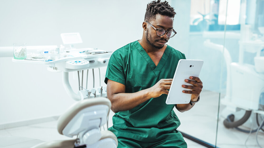 Dentist in Green Scrubs Using Tablet in Modern Dental Clinic Consultation and Record Review