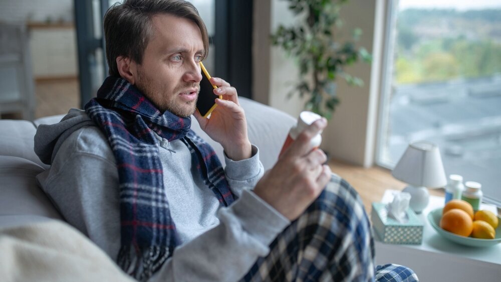 Man wearing scarf speaking with doctor on phone Doctor on phone. Dark-haired sick man wearing scarf speaking with doctor on phone