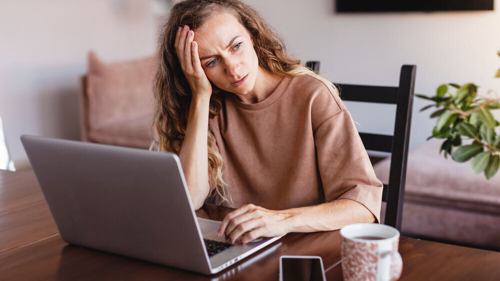Junge Frau sitzt vor dem Laptop und fühlt sich krank, wirkt abgeschlagen und gestresst. Junge Frau sitzt vor dem Laptop und fühlt sich krank, wirkt abgeschlagen und gestresst.