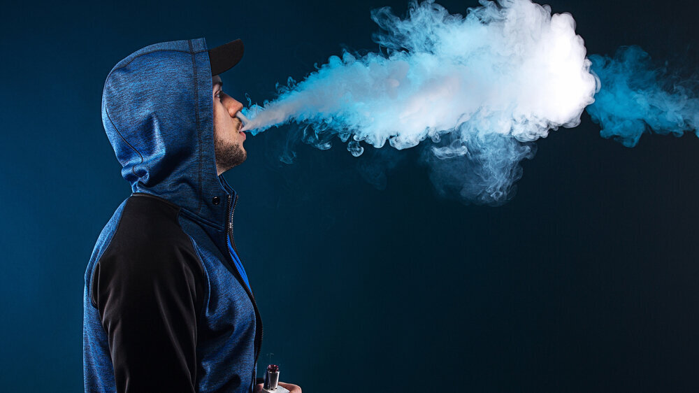 vaping man holding a mod. A cloud of vapor. dark blue background.