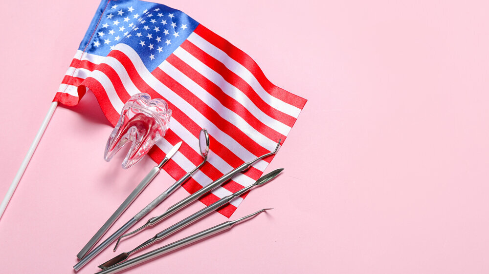 Dental tools with plastic tooth and USA flag on pink background Dental tools with plastic tooth and USA flag on pink background