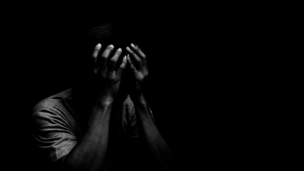 Man sitting alone felling sad worry or fear and hands up on head on black background Man sitting alone felling sad worry or fear and hands up on head on black background