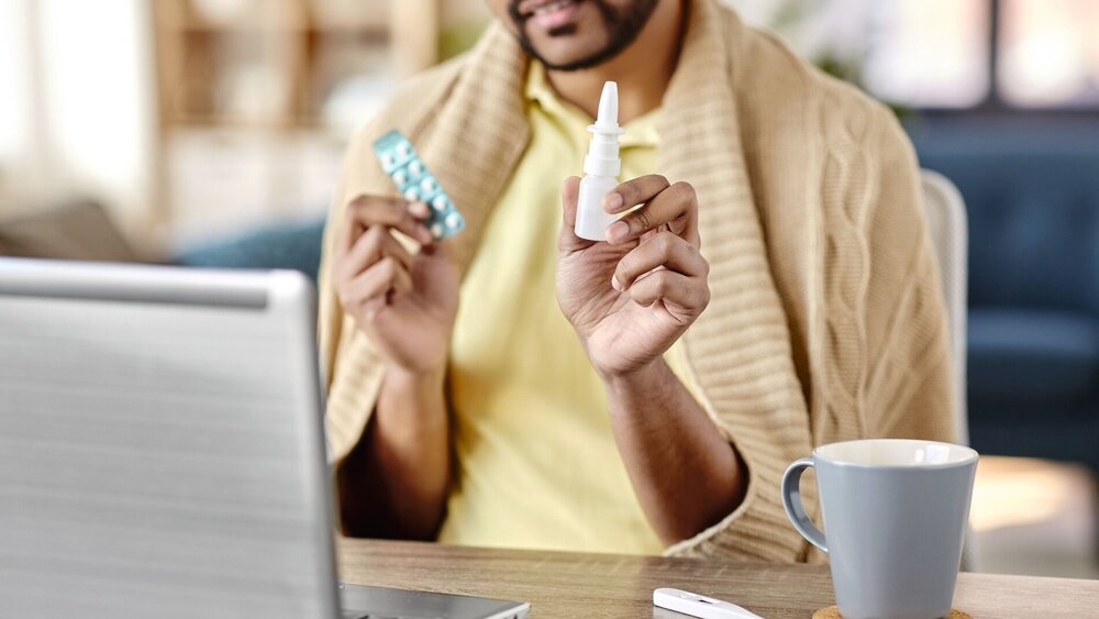 healthcare, technology and people concept - sick indian man in blanket with thermometer having video call on laptop computer at home