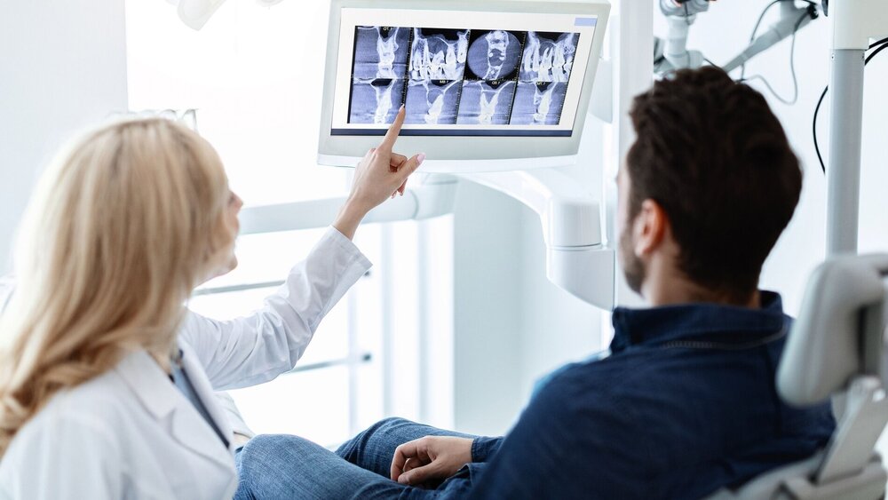 Zahnärztin zeigt im Gespräch mit einem Patienten auf einen Monitor